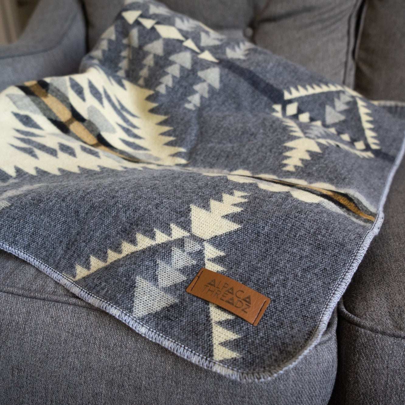 Andean Alpaca Wool Blanket - Cloud with vibrant reversible patterns on a grey sofa.