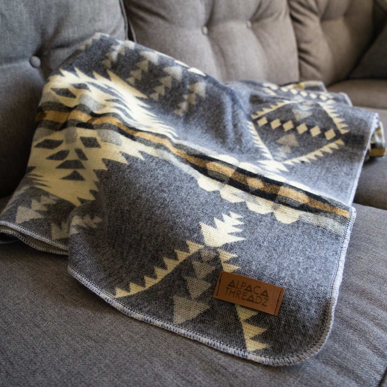Andean Alpaca Wool Blanket in Cloud pattern on a gray couch, showcasing reversible design and artisan craftsmanship.