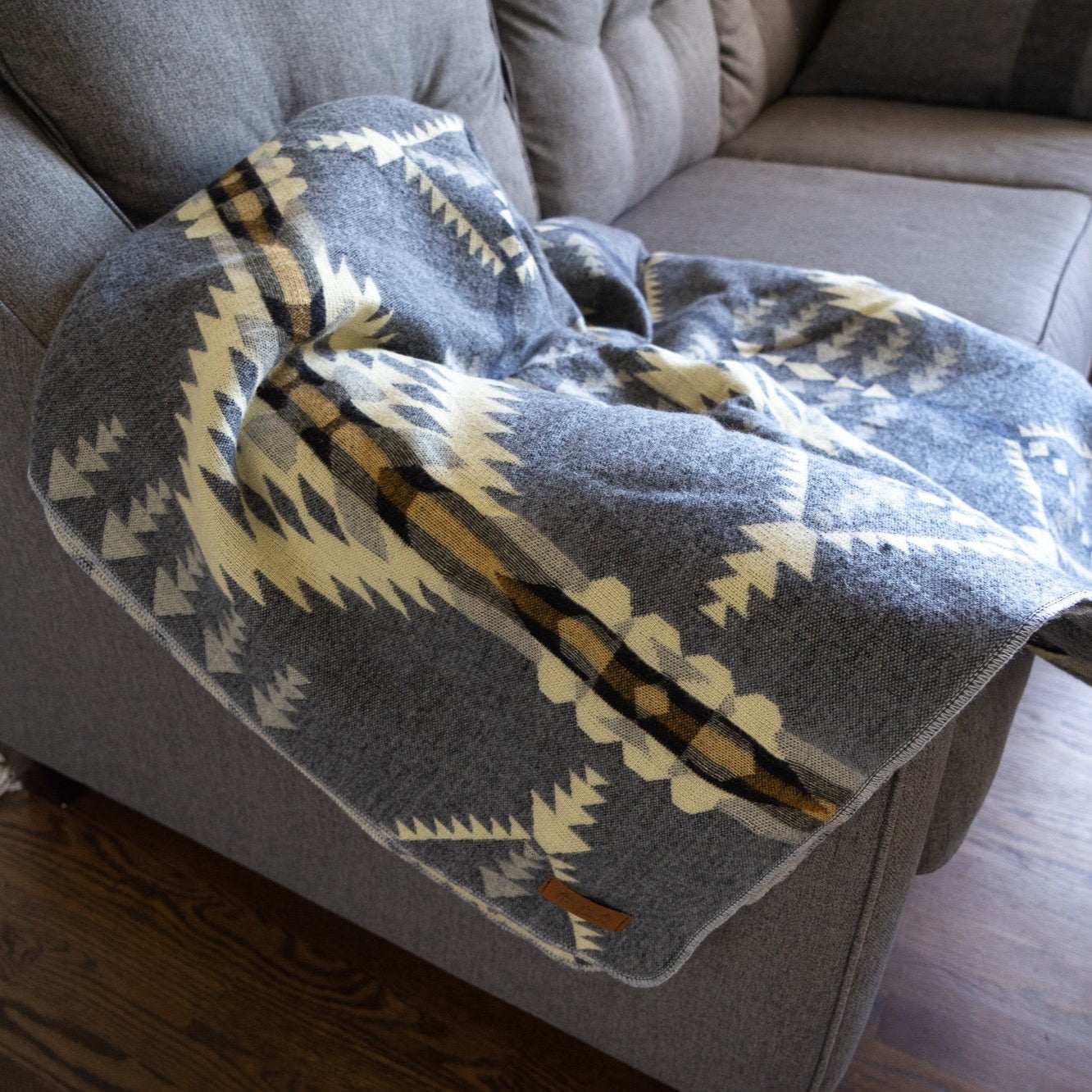 Andean Alpaca Wool Blanket - Cloud on a sofa, showcasing its reversible design and vibrant patterns.