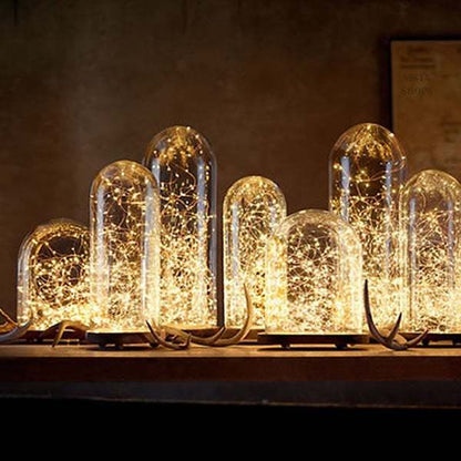 Mini Fiery 100 solar-powered string lights illuminating in glass domes on a table.