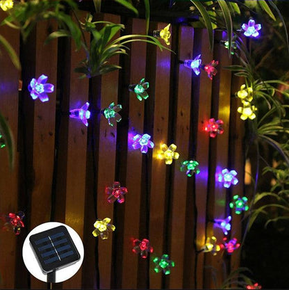 Cherry Blossom Solar LED String Lights on a wooden fence with a solar panel.