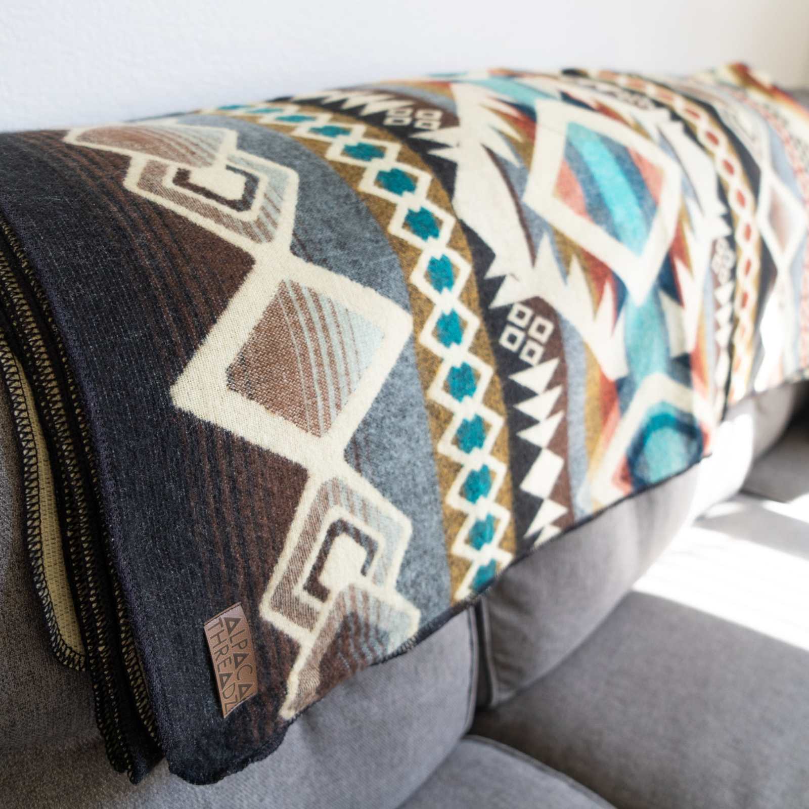 Andean Alpaca Wool Blanket with Inca designs, reversible and handmade in Ecuador, displayed on a sofa.