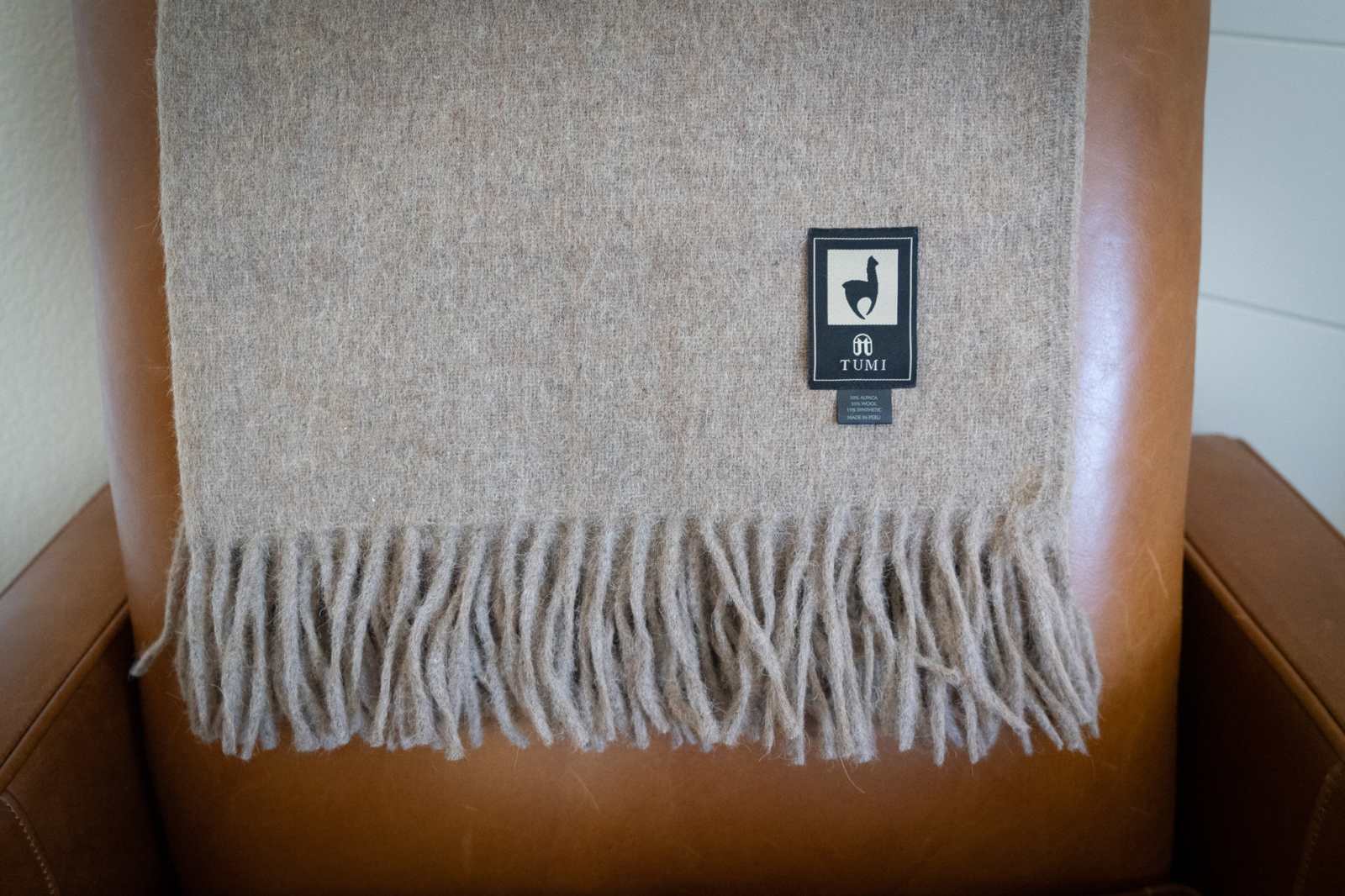 Alpaca Wool Throw Blanket in solid tan color with fringe, made from Peruvian alpaca and wool blend, displayed on a chair.