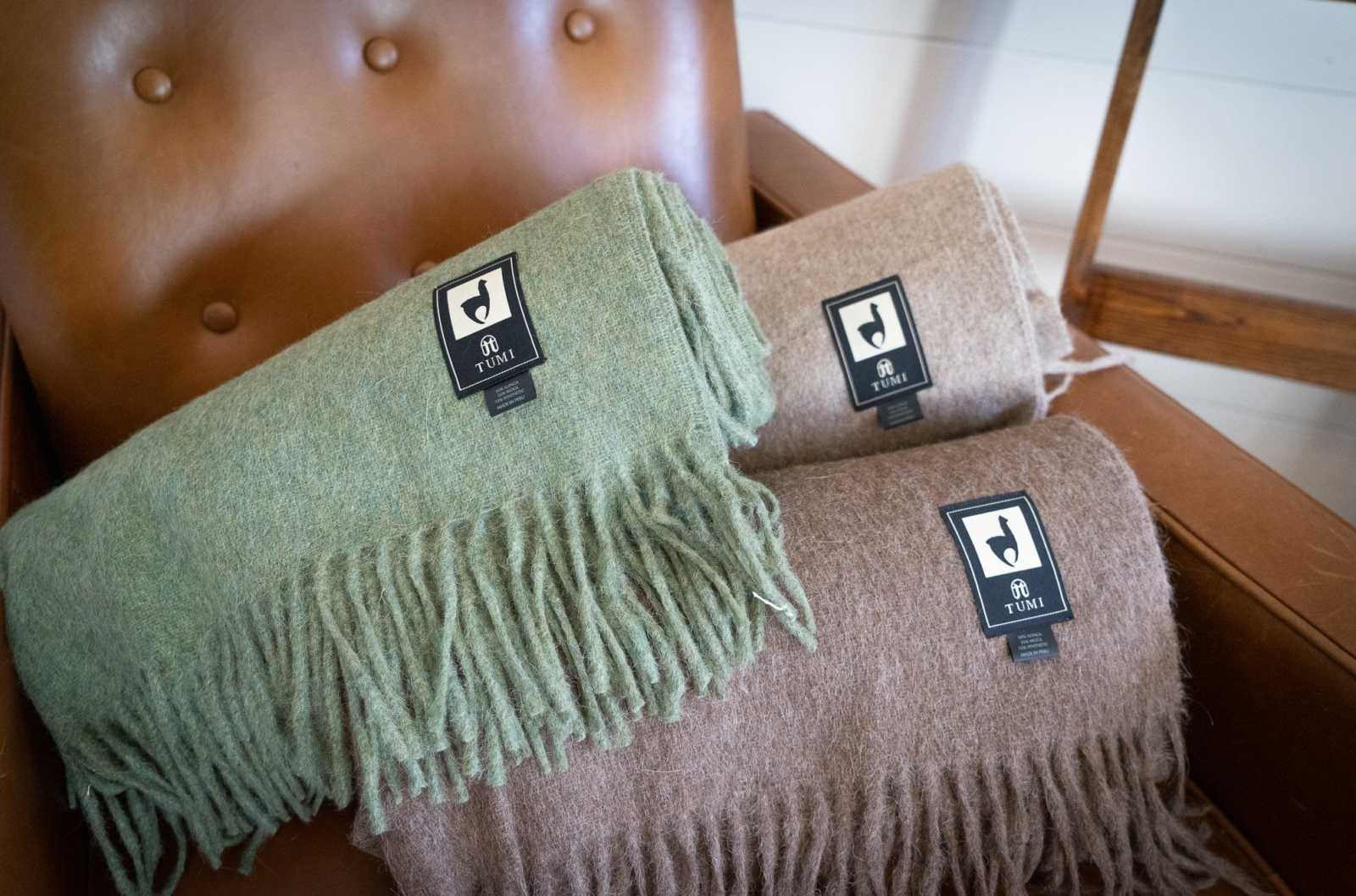 Alpaca wool throw blankets with fringe in green and tan colors on a brown chair.