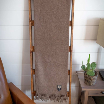 Alpaca wool throw blanket in solid brown with fringe, displayed on a wooden ladder.