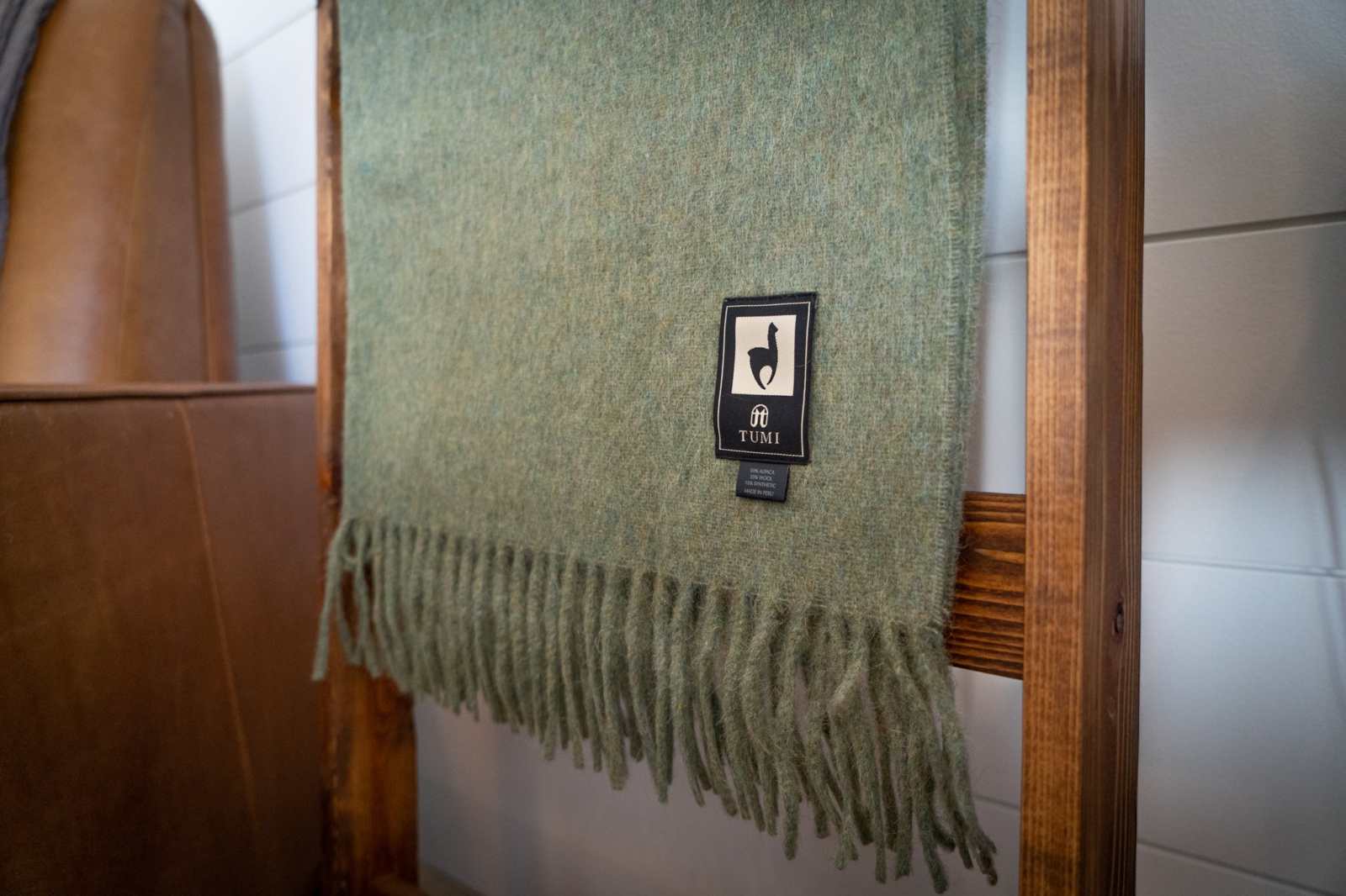 Alpaca Wool Throw Blanket in green with fringed edges hanging on a wooden rack.