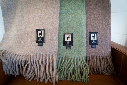 Alpaca wool throw blankets in solid colors with fringe detail displayed on a couch.