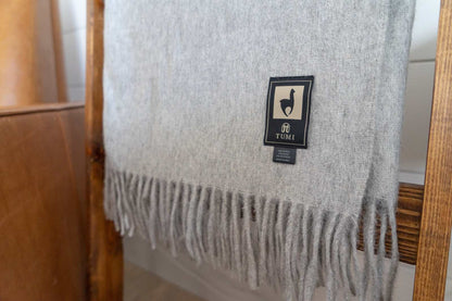 Alpaca wool throw blanket in solid light gray with fringe edges.