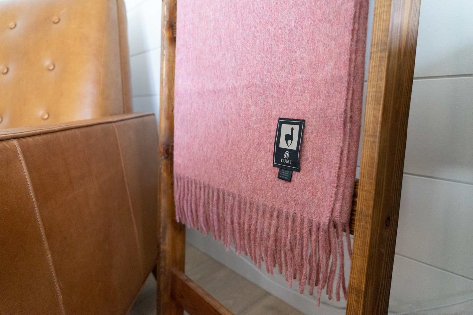 Alpaca wool throw blanket with fringe in solid color on display next to leather chair.