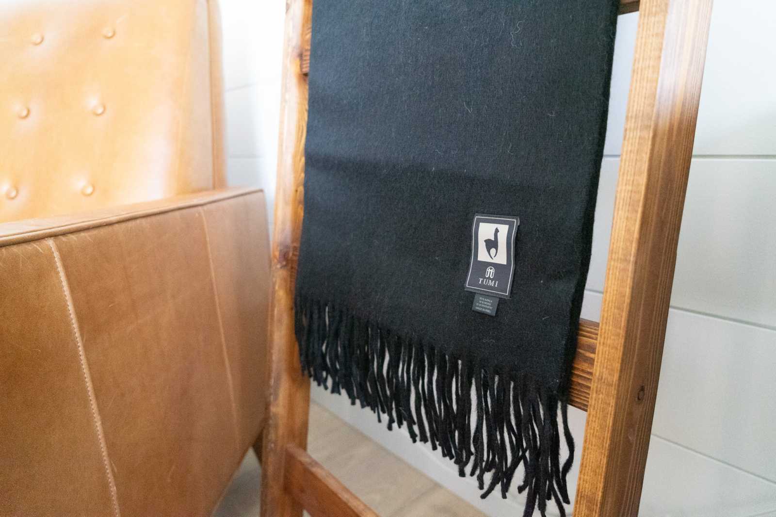 Alpaca wool throw blanket with fringe in solid black displayed on wooden chair.