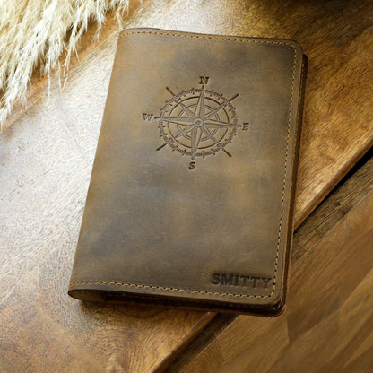 Handcrafted leather journal with a compass design and personalized engraving on a wooden surface.