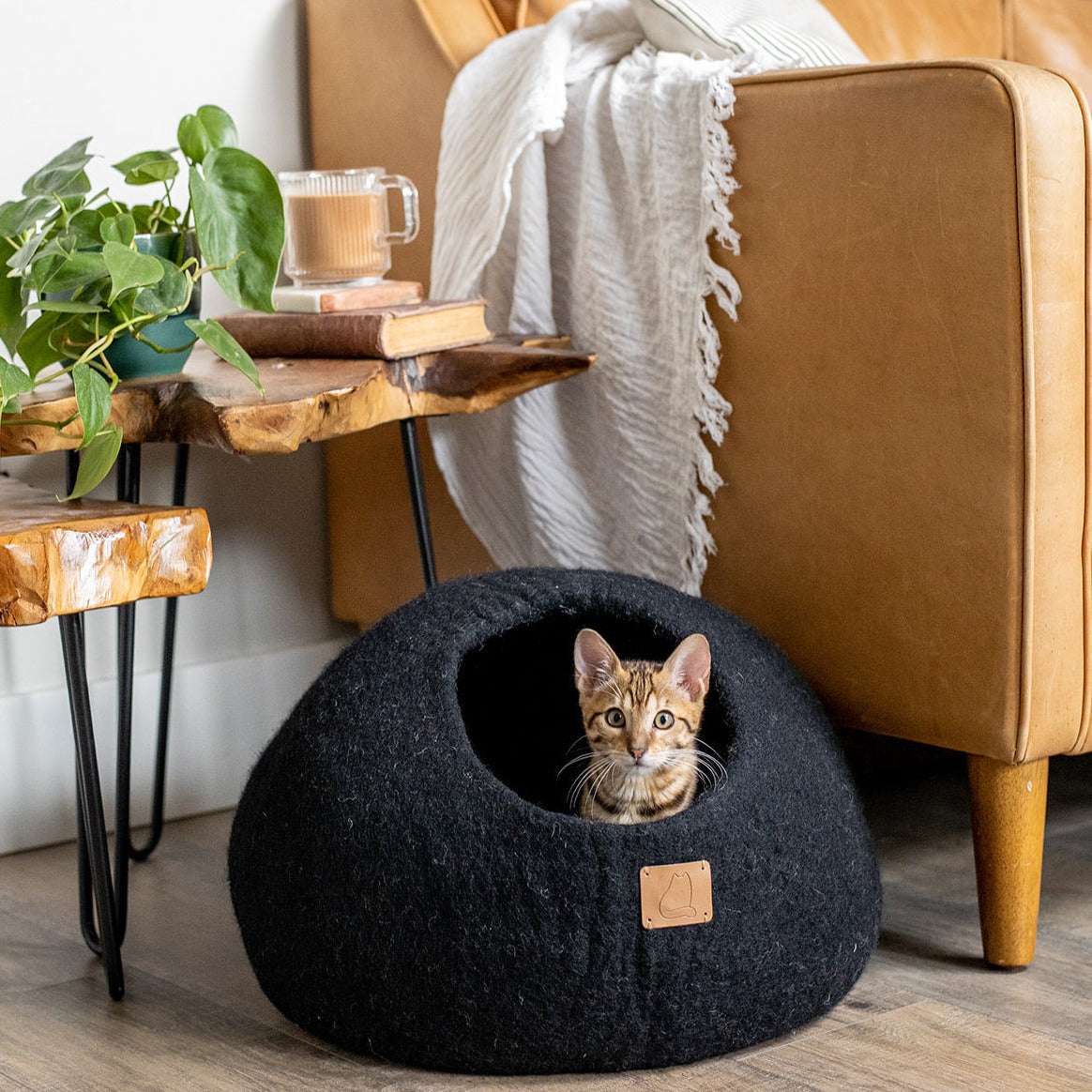 Round style felted wool cat cave bed in night black with a cat lounging inside, placed in a cozy living room setting.