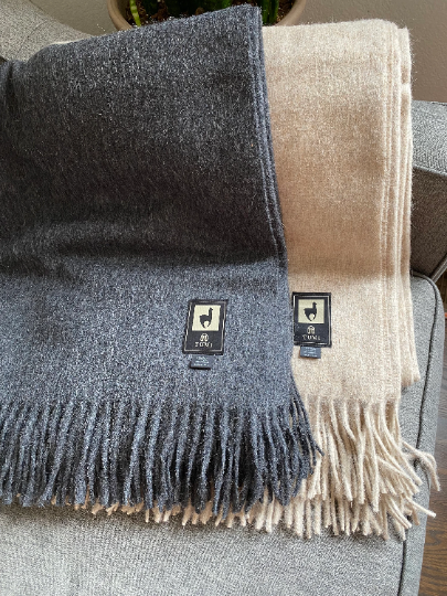 Alpaca wool throw blankets in gray and tan with fringe edges, displayed on a couch.